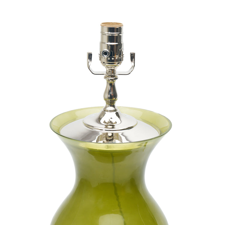 A close-up of a table lamp featuring green glass, a lucite base, and a polished silver metal socket, set against a plain white background.
