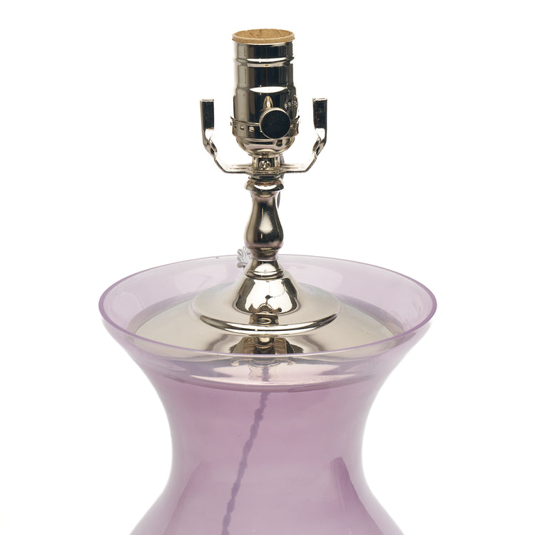 A close-up of a table lamp featuring purple glass, a lucite base, and a polished silver metal socket, set against a plain white background.