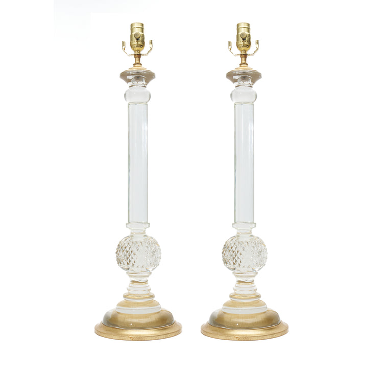A pair of elegant table lamps with clear glass columns, textured lower globes, and polished gold-finished bases and lamp fittings, shown against a plain white background.