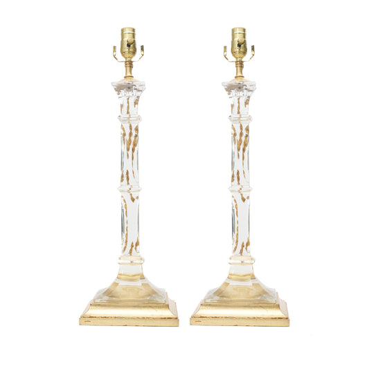 A pair of table lamps with clear glass columns, gold-finished bases, and bulb sockets, shown against a plain white background.