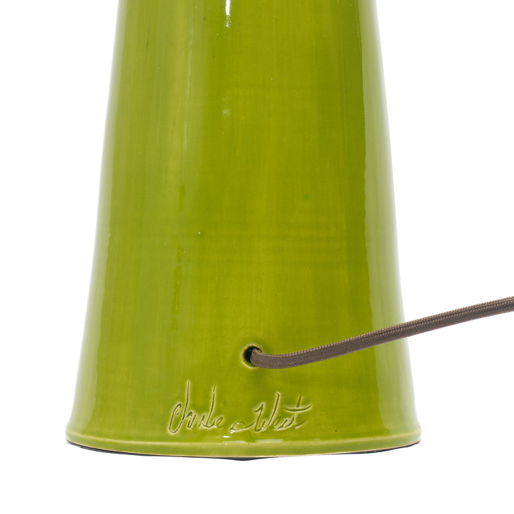 Close-up of the base of a glossy olive green ceramic lamp, showing a brown cord entering a hole and an embossed script logo near the bottom.