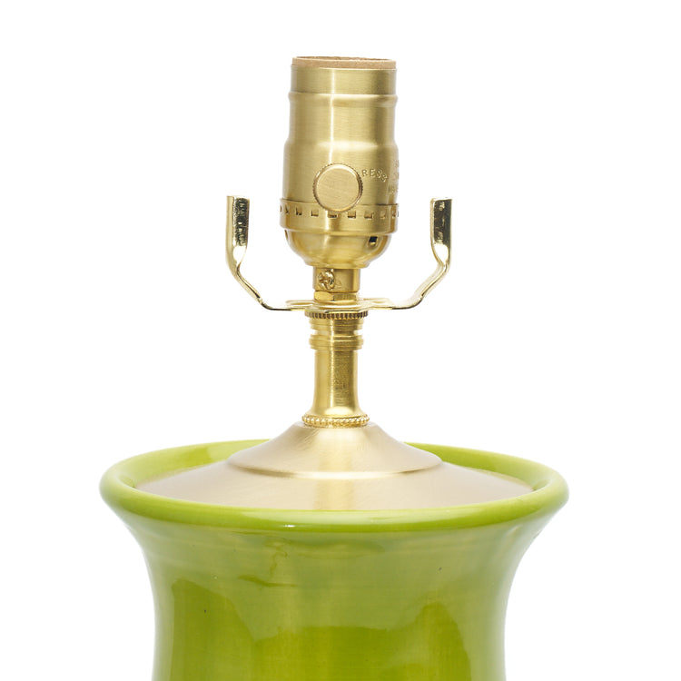 Close-up of a table lamp featuring a glossy lime green ceramic base and a polished brass lamp socket and shade on a white background.