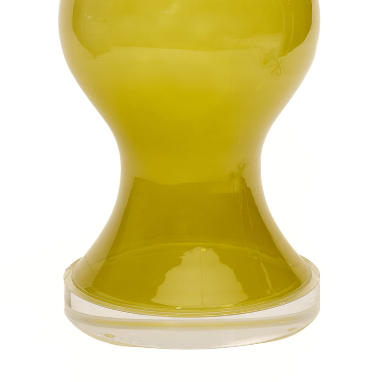 A close-up of a citron green glass lamp with a lucite circular base, photographed against a white background.