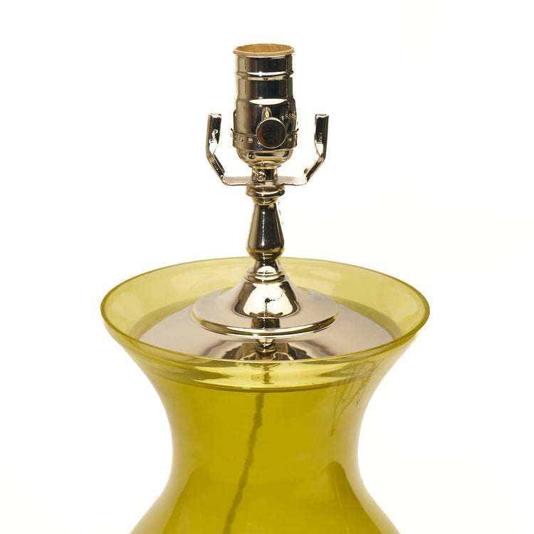 A close-up of a table lamp featuring citron green glass, a lucite base, and a polished silver metal socket, set against a plain white background.