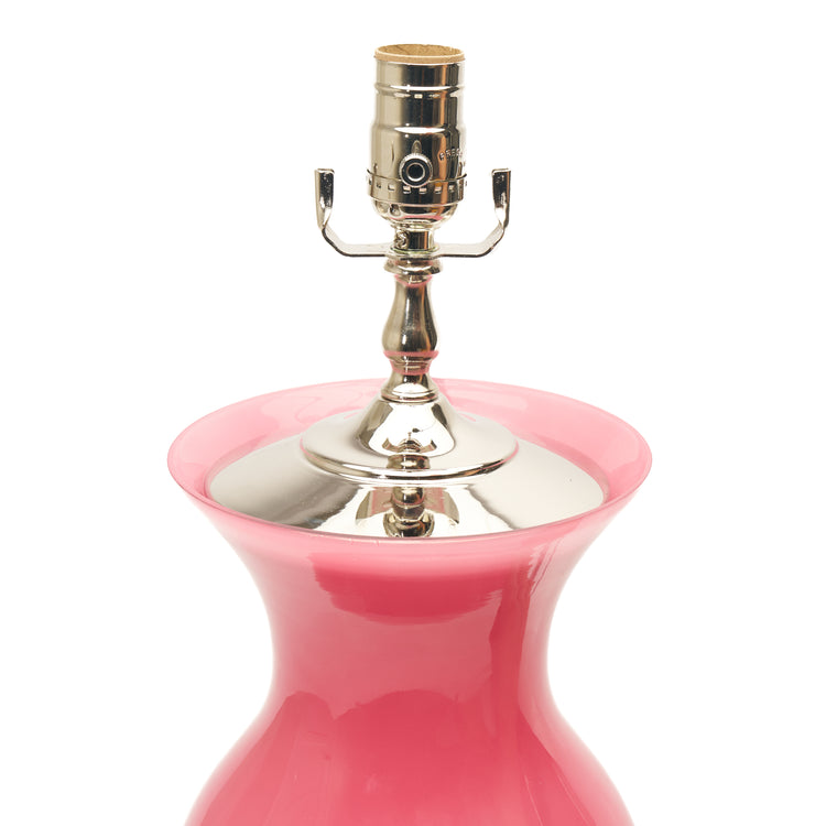 A close-up of a table lamp featuring pink conch glass, a lucite base, and a polished silver metal socket, set against a plain white background.