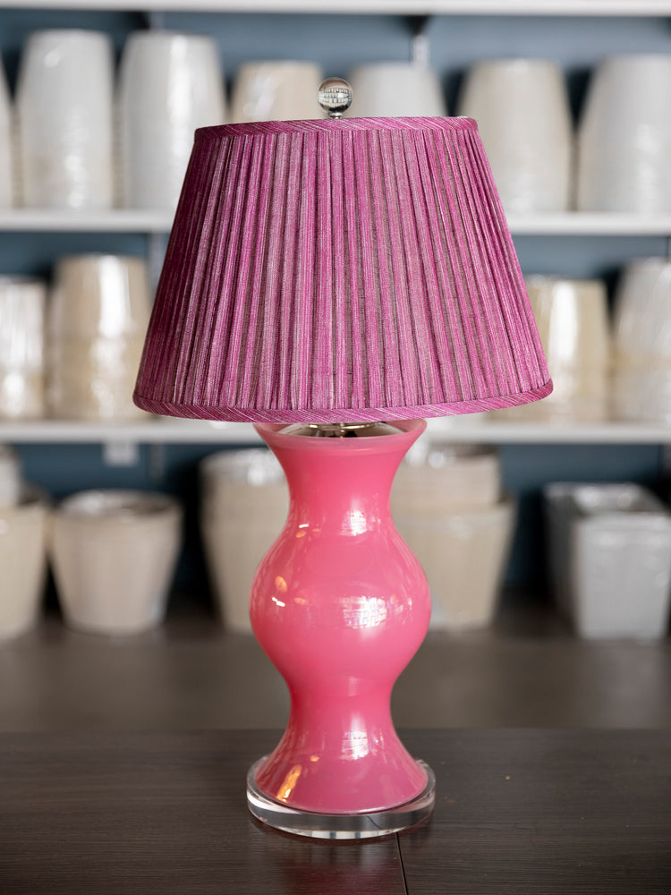 A pink table lamp with a glossy pink ceramic base and a pleated pink fabric lampshade