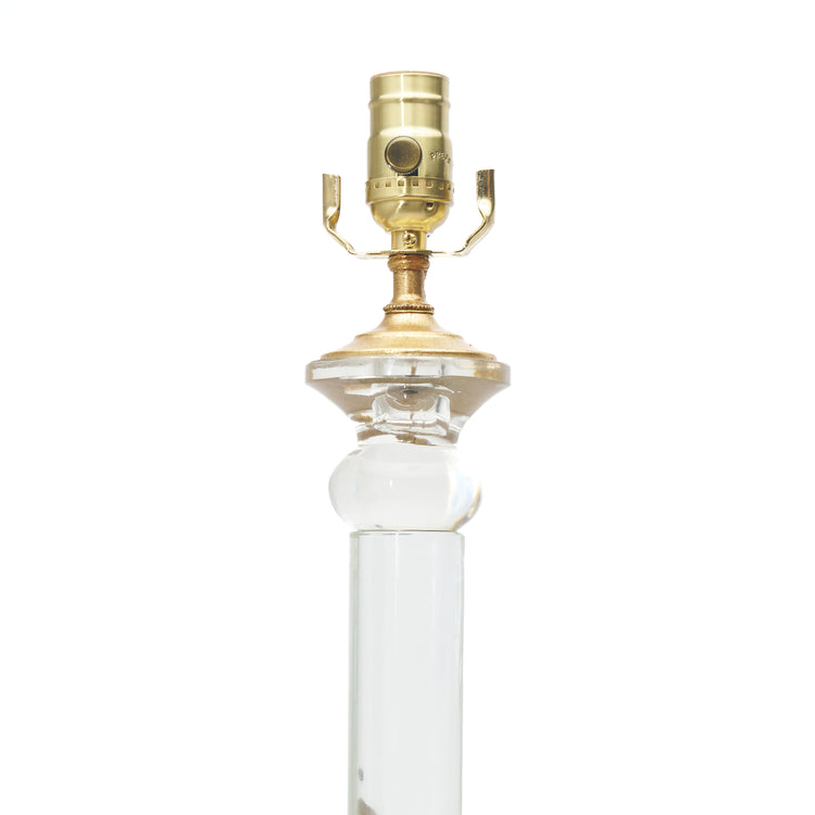 The top of an elegant table lamp with clear glass columns, textured crystal-like lower globes, and polished gold-finished bases and lamp fittings, shown against a plain white background.