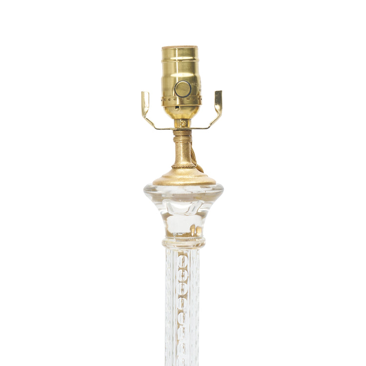 A close-up of a table lamp base featuring a clear glass stem and a polished brass socket, isolated on a white background.