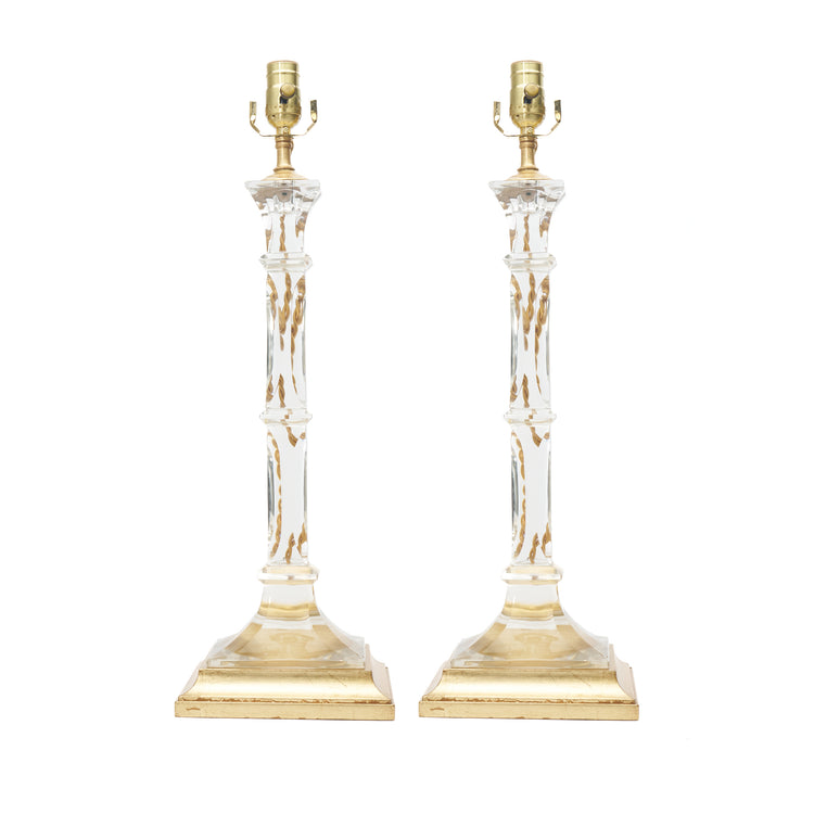A pair of table lamps with clear glass columns, gold-finished bases, and bulb sockets, shown against a plain white background.