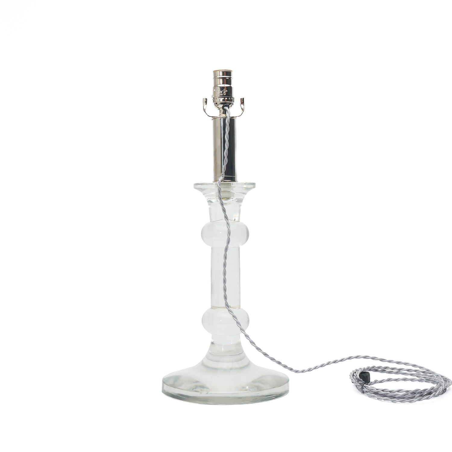Clear glass table lamp base with a silver metal socket and a silver braided cord on a white background.