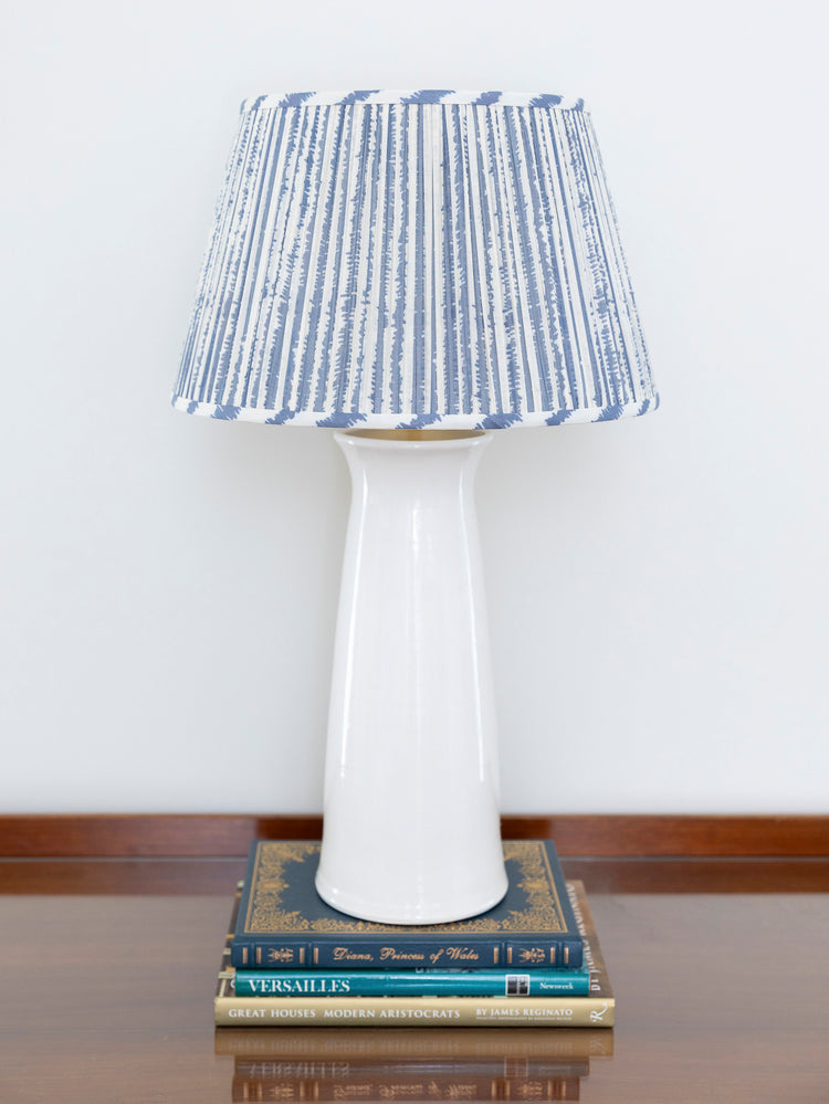 A table lamp with a glossy white ceramic base and a blue-and-white vertically striped fabric shade