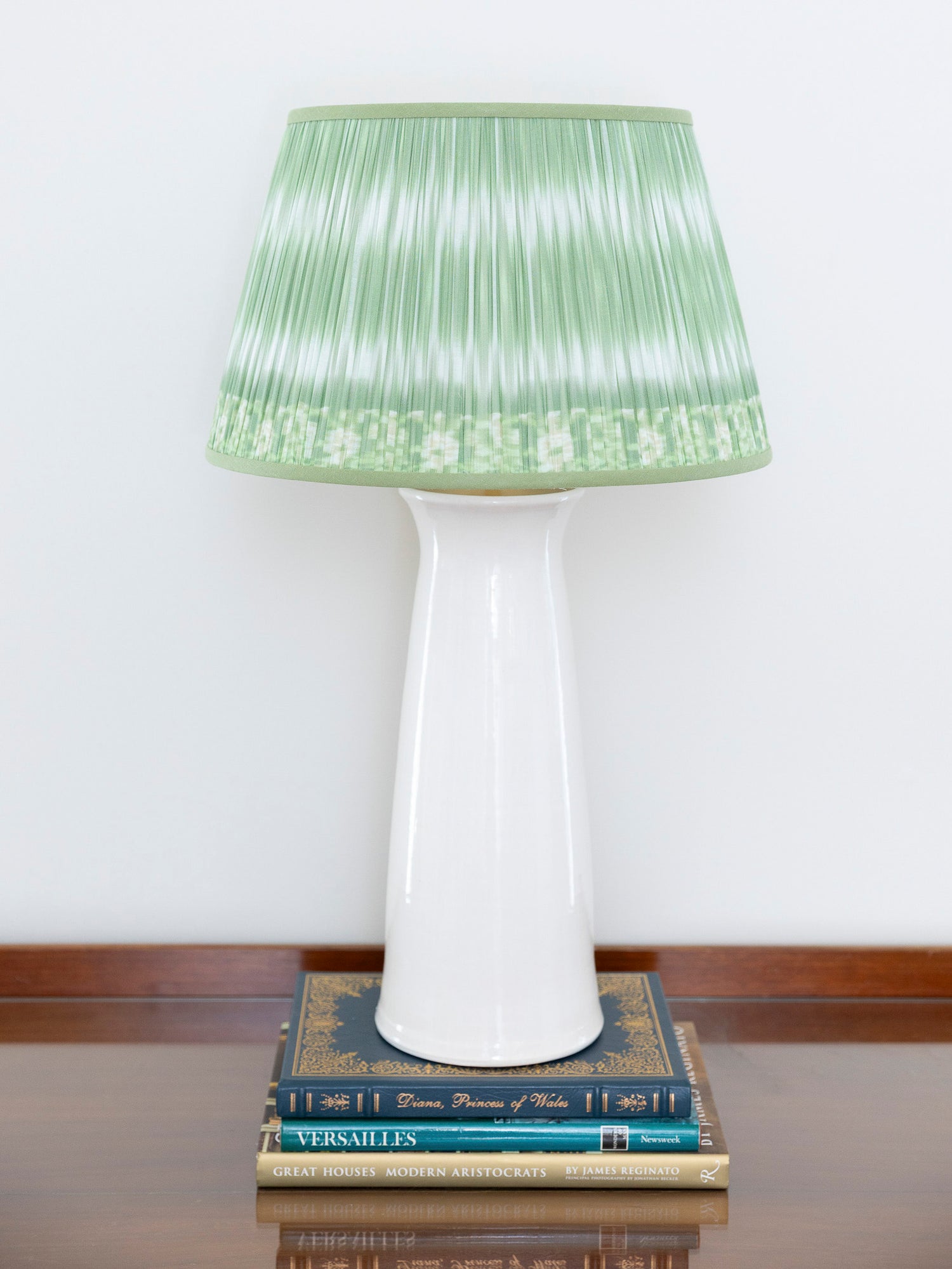 A table lamp with a white ceramic base and a pleated light green shade