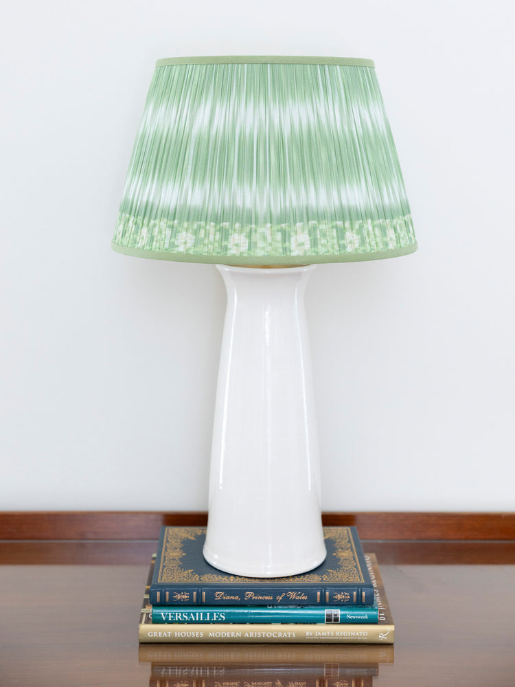 A table lamp with a white ceramic base and a pleated light green shade